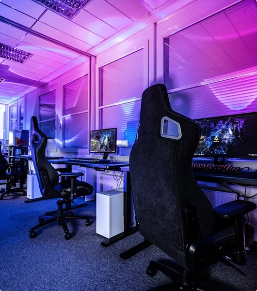 Moderne esports-gameruimte met professionele gamestoelen, computers en sfeervolle paarse verlichting.